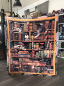 Das Produktbild zeigt eine Decke mit einem Bücherregal, in dem drei unterschiedliche Katzen zwischen Büchern schlafen.